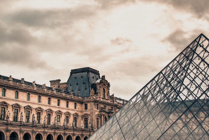 The outside of the Lourve on a cloudy day.